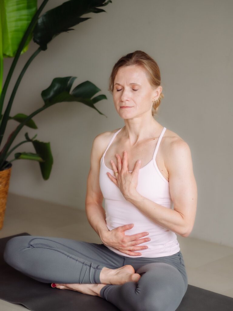 Yogalehrerin Ela Buchholz – Meditationssitz im Schneidersitz, Augen geschlossen, eine Hand auf Herz, eine auf Bauch